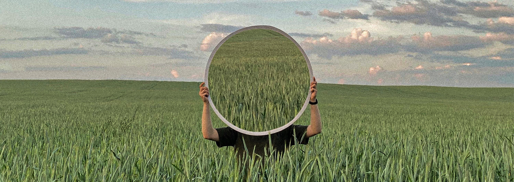 A person holding a mirror over their face in the middle of a vibrant flower field, with the reflection showing the same flower field, symbolizing introspection and the interconnectedness of nature and business.